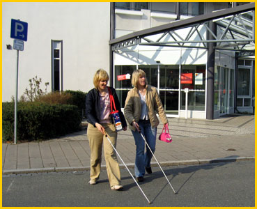 Bild: zwei blinde Personen machen selbständig einen Stadtbummel. Dank einer Schulung in Orientierung und Mobilität kein Problem.